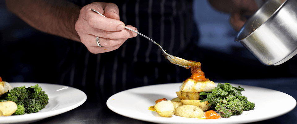 Mano de un chef agregando salsa a una receta salada con una cuchara plateada