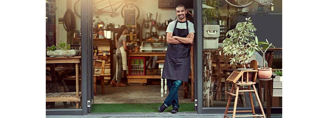 Hombre con mandil negro en la puerta de su cafetería