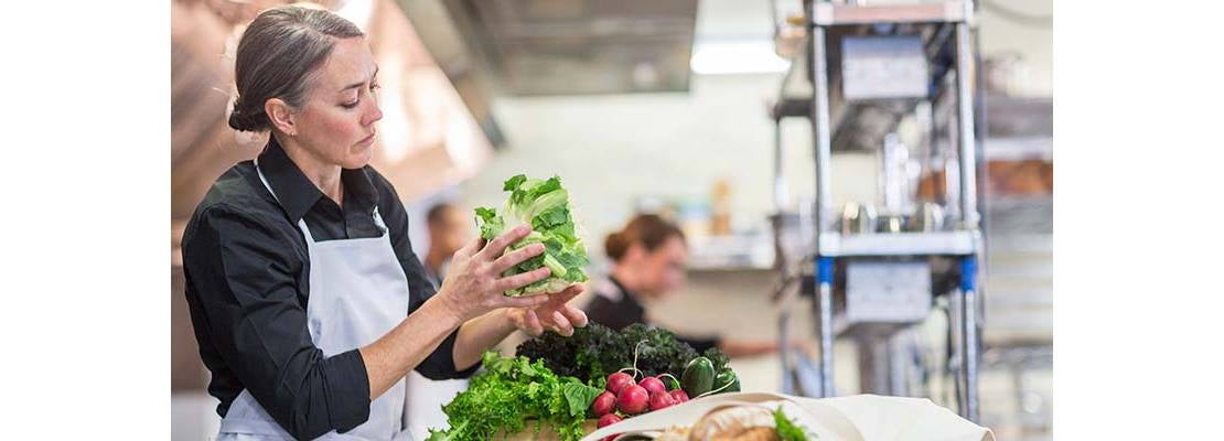 Mujer en cocina profesional con una lechuga en la mano alistando las verduras