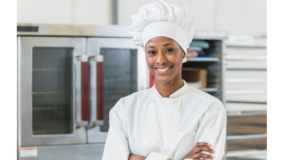 Una chef morena con toque y mandil sonriendo en su cocina