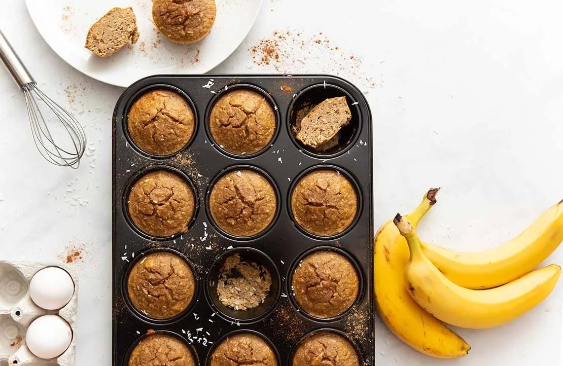 Muffins sin gluten en molde para hornear, con batidor, huevos y plátanos