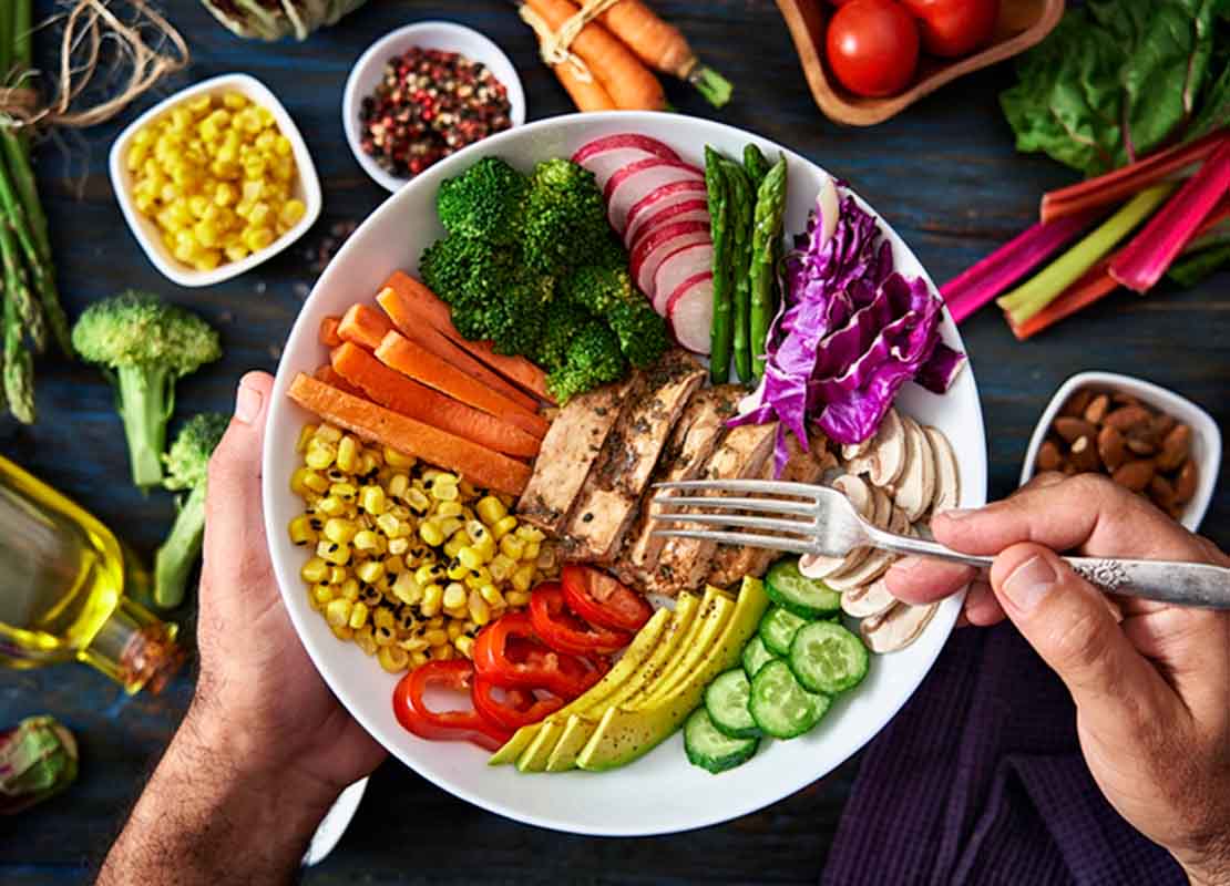 Manos de hombre sosteniendo plato de ensalada con diferentes ingredientes