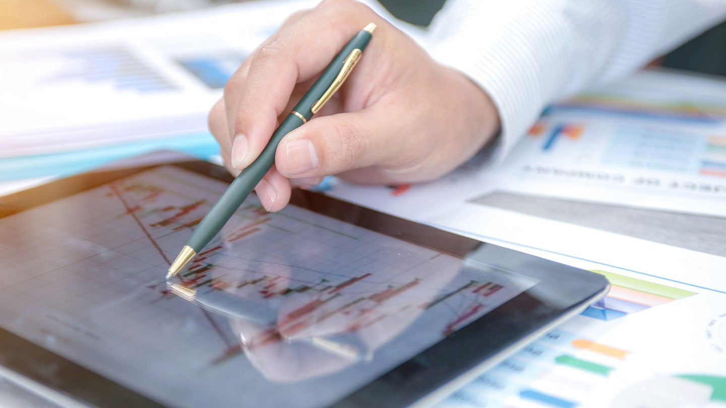 Mano con lapicero sobre una tablet con información sobre los costos fijos y variables