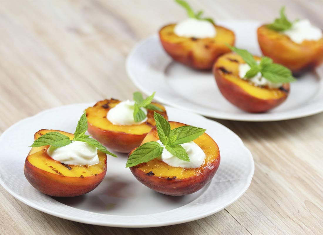 Dos platos con postre de melocotones a la plancha con crema batida