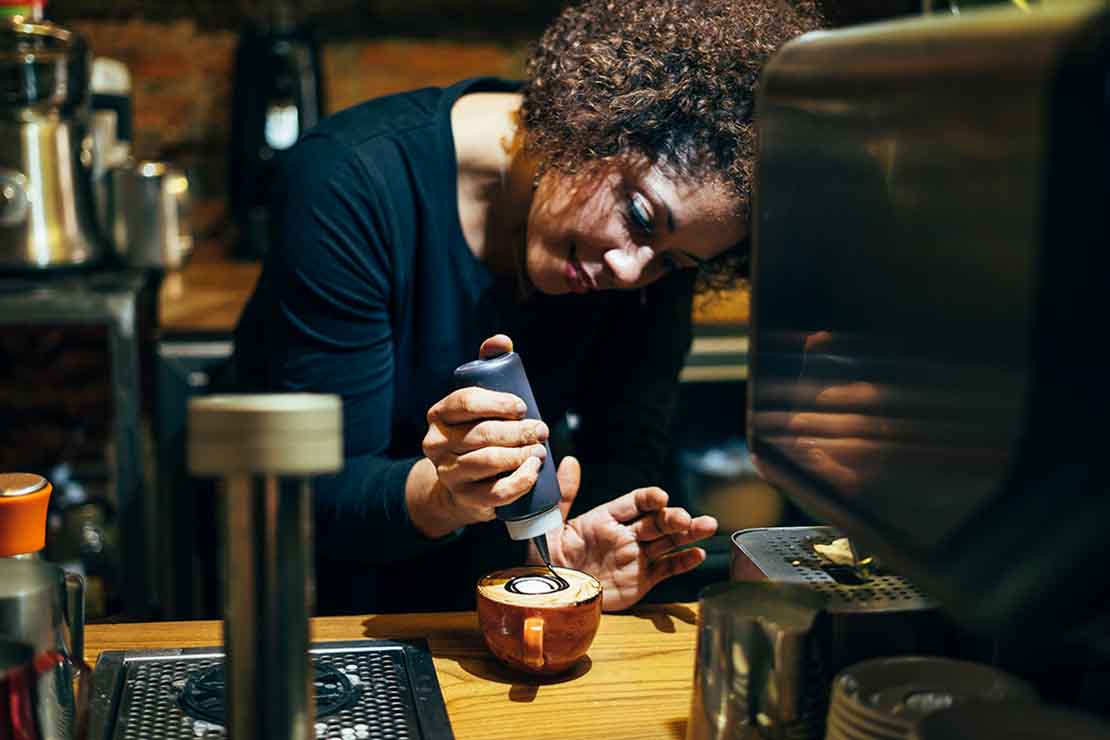 Experta en café decora una bebida de especialidad en su cafetería utilizando salsa de chocolate