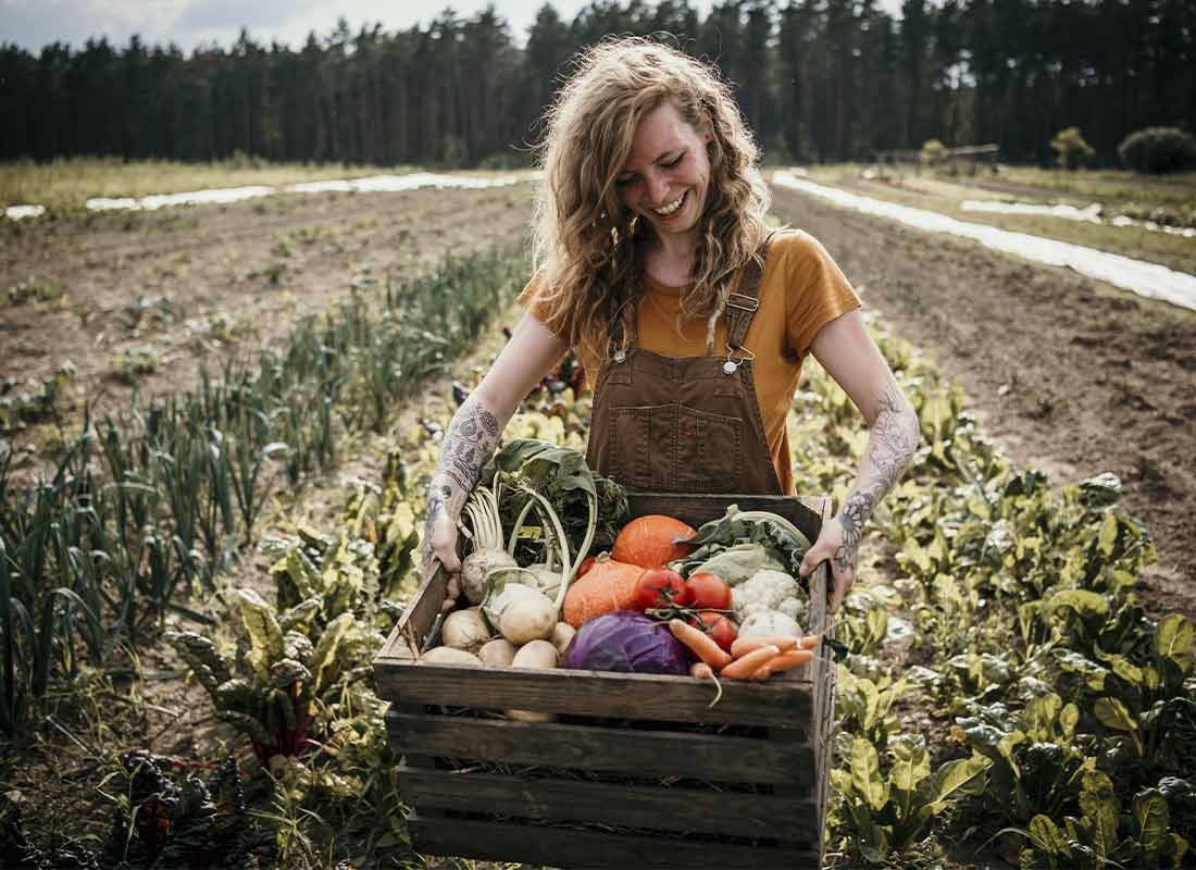 Mujer en cultivo sosteniendo una caja con verduras de temporada