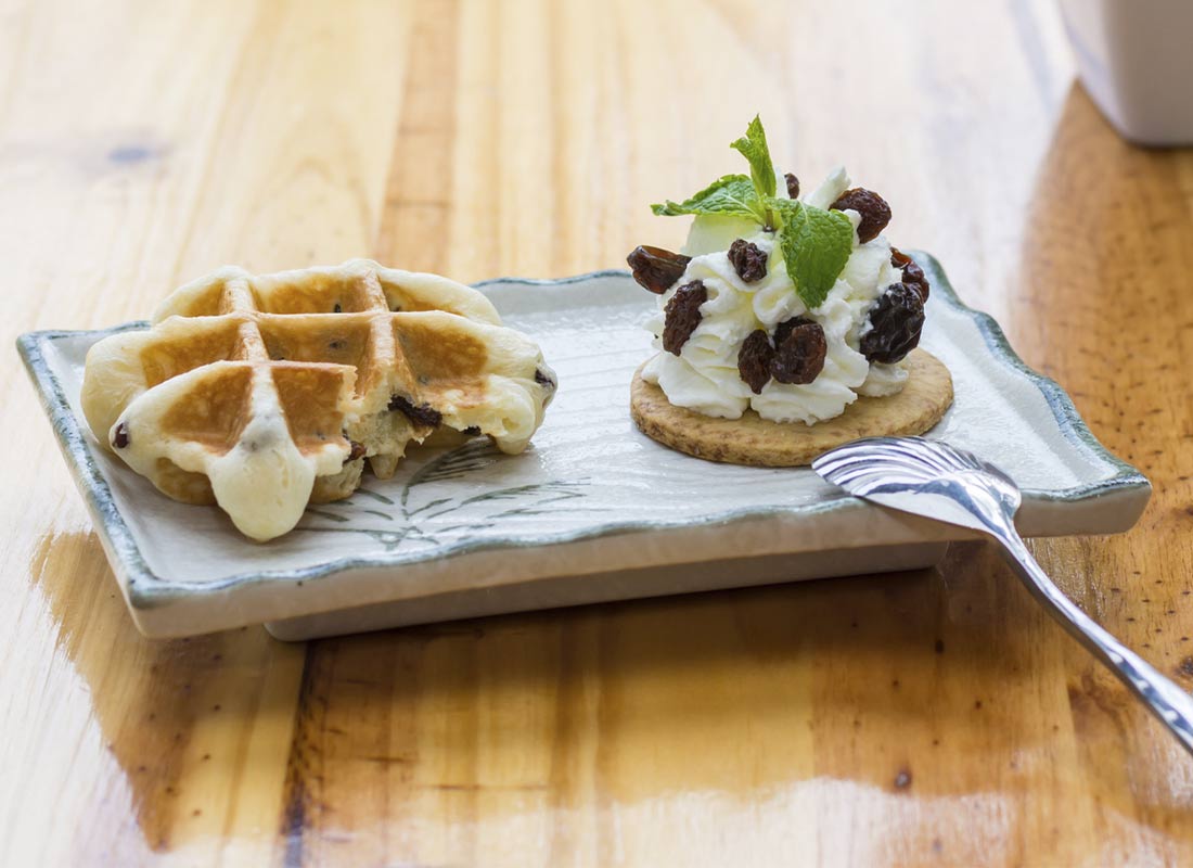 Postre para compartir de waffle relleno y galleta con crema batida y uvas pasas