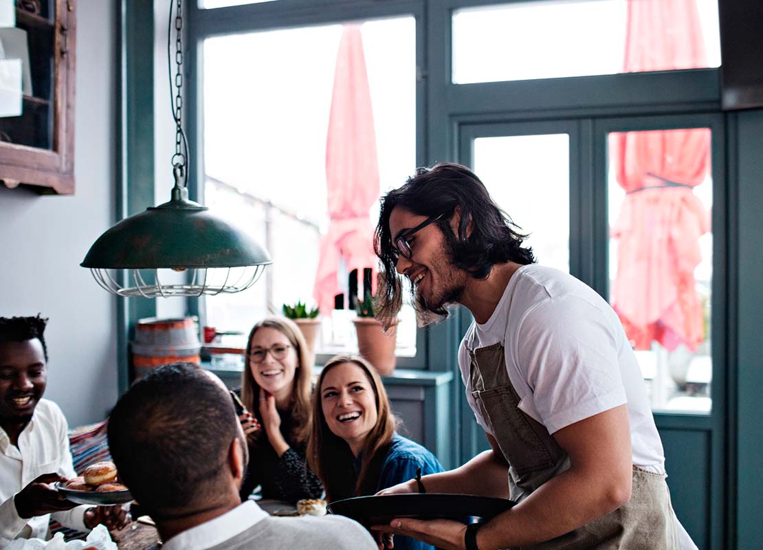 Con una capacitación de personal un mesero atiende amable y asertivamente a un grupo de clientes en un restaurante