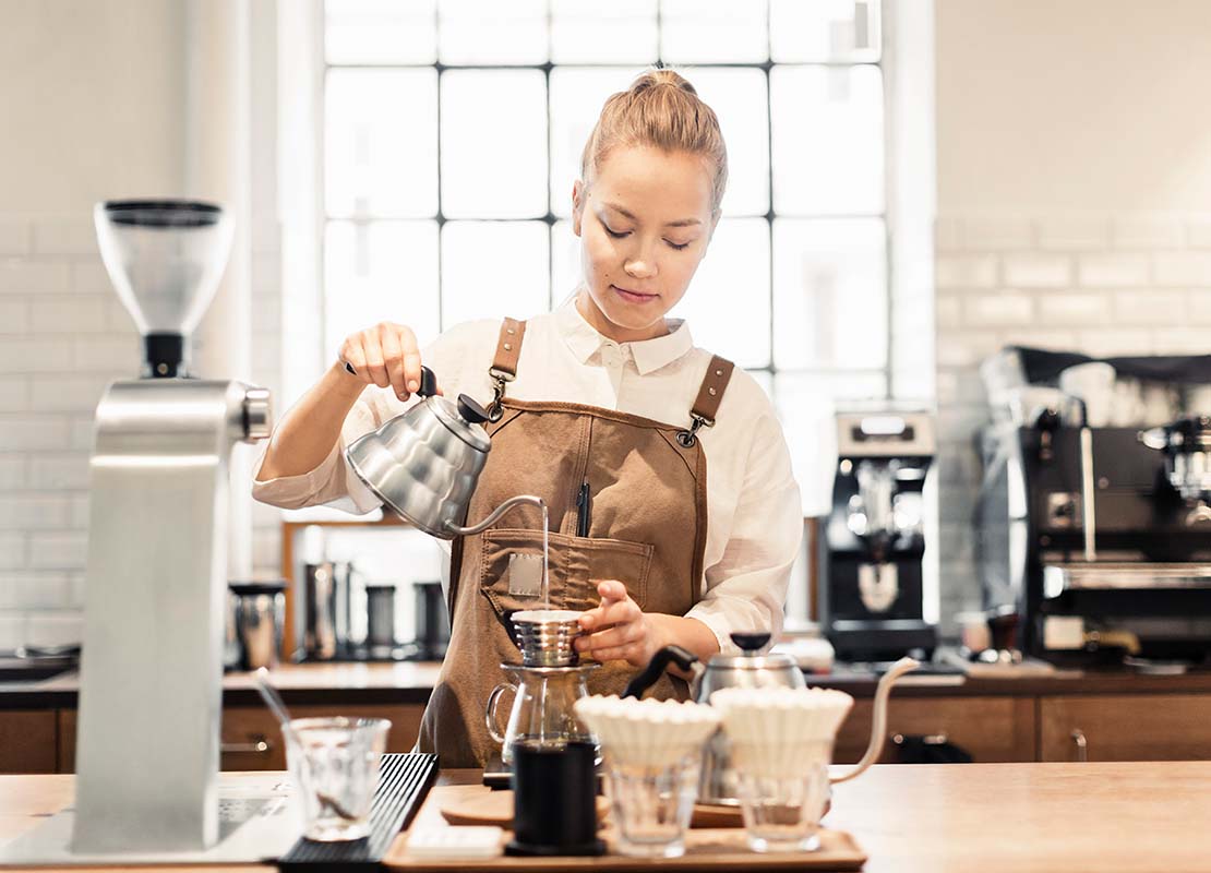 Una barista prepara café con el método de filtrado utilizando dripper en una cafetería tras recibir capacitación de personal