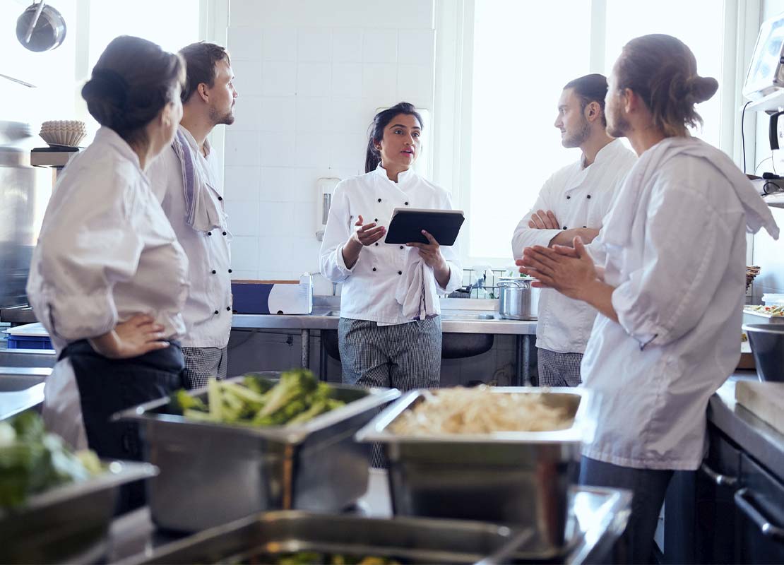 Cuatro cocineros en torno a la chef ejecutiva se reúnen en la cocina y evalúan temas de seguridad, organización y gestión