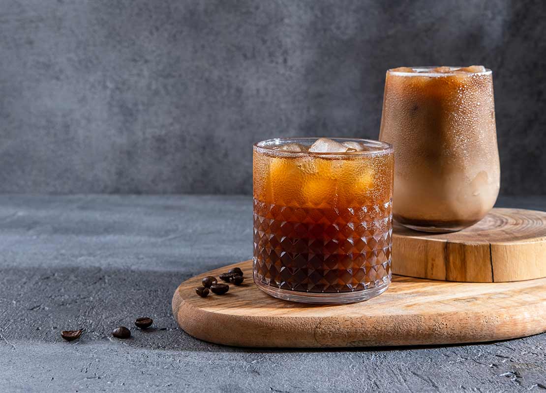 Sobre una tabla con dos niveles se ubican dos vasos diferentes con bebidas de café frío preparadas de forma distinta