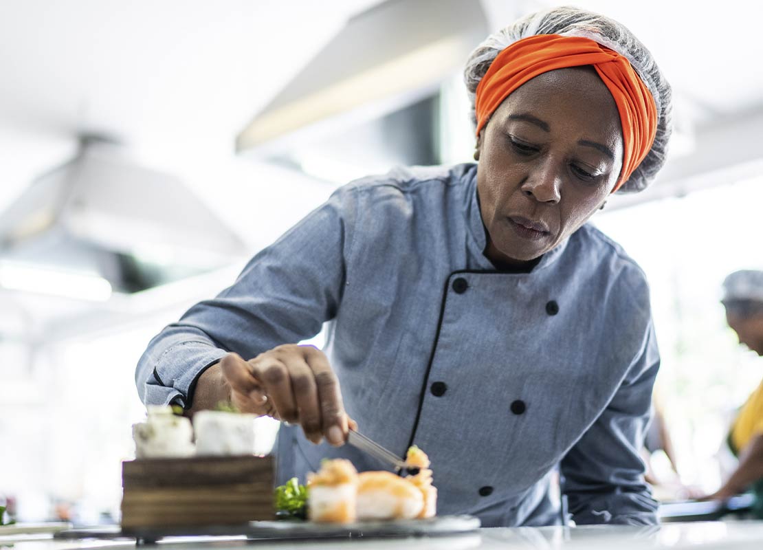 En una cocina de restaurante, una chef decora cuidadosamente un platillo que será fotografiado con técnicas de food styling