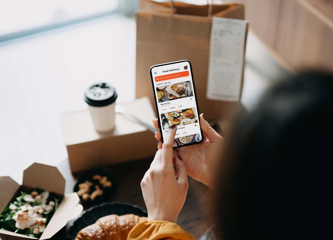 Mujer con dos cajas de comida y una bebida al frente revisa en su app de delivery que su entrega a domicilio sea correcta