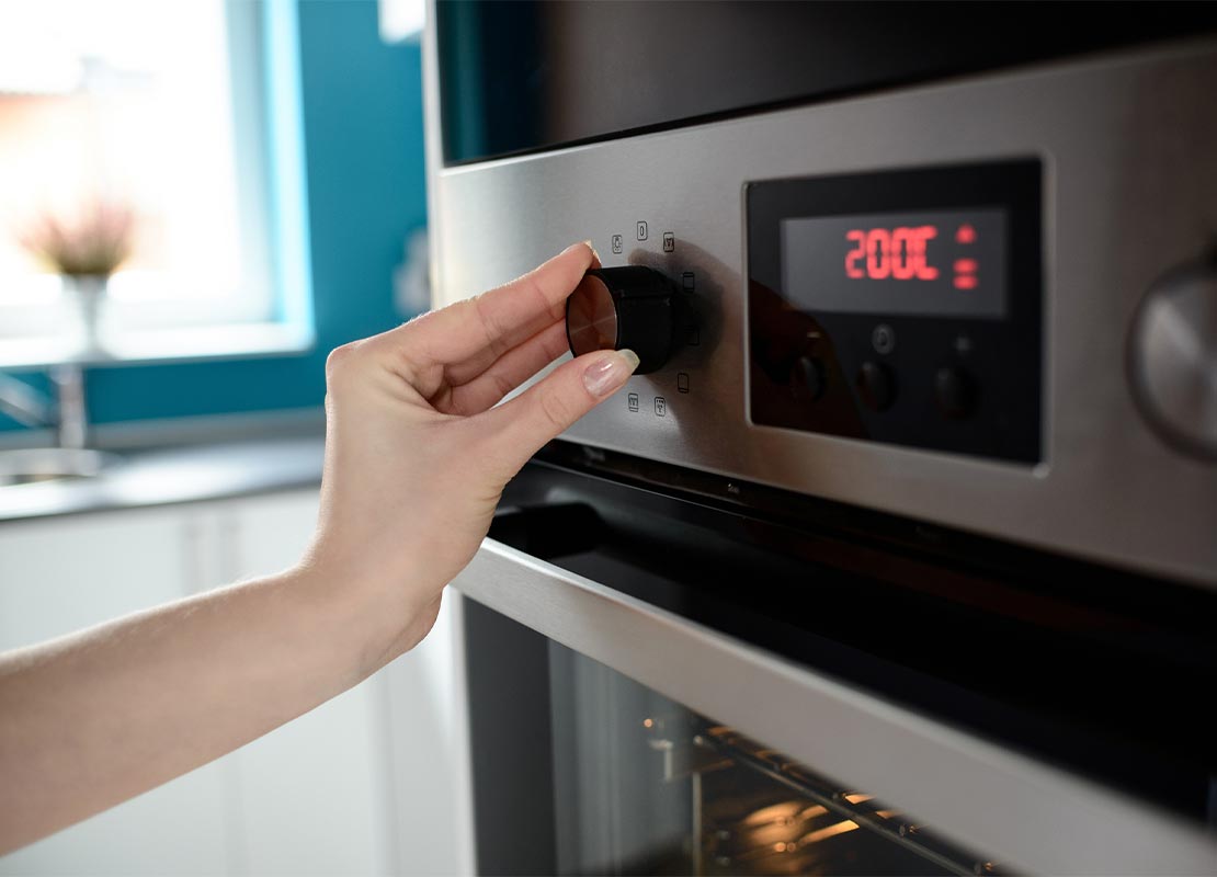 Mujer ajusta la temperatura de un horno industrial que hace parte de un equipamiento de cocina