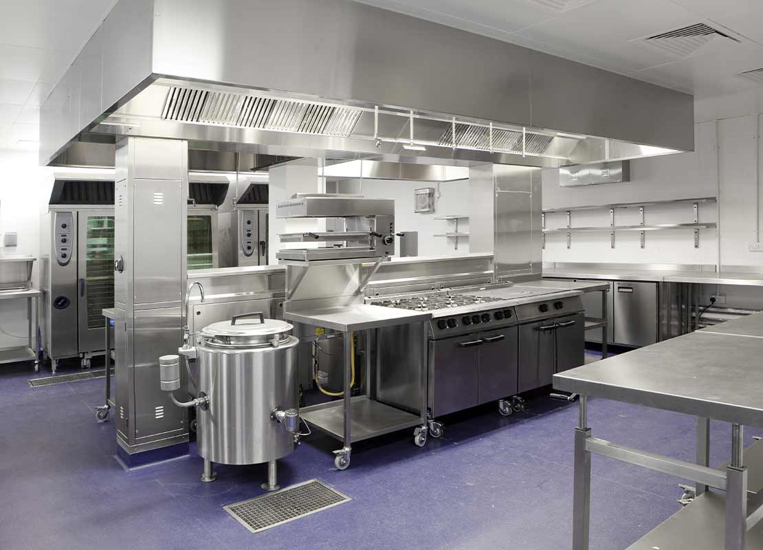 Cocina industrial con equipamiento de cocina en acero inoxidable que incluye hornos, mesas, mezcladoras, neveras, etc.