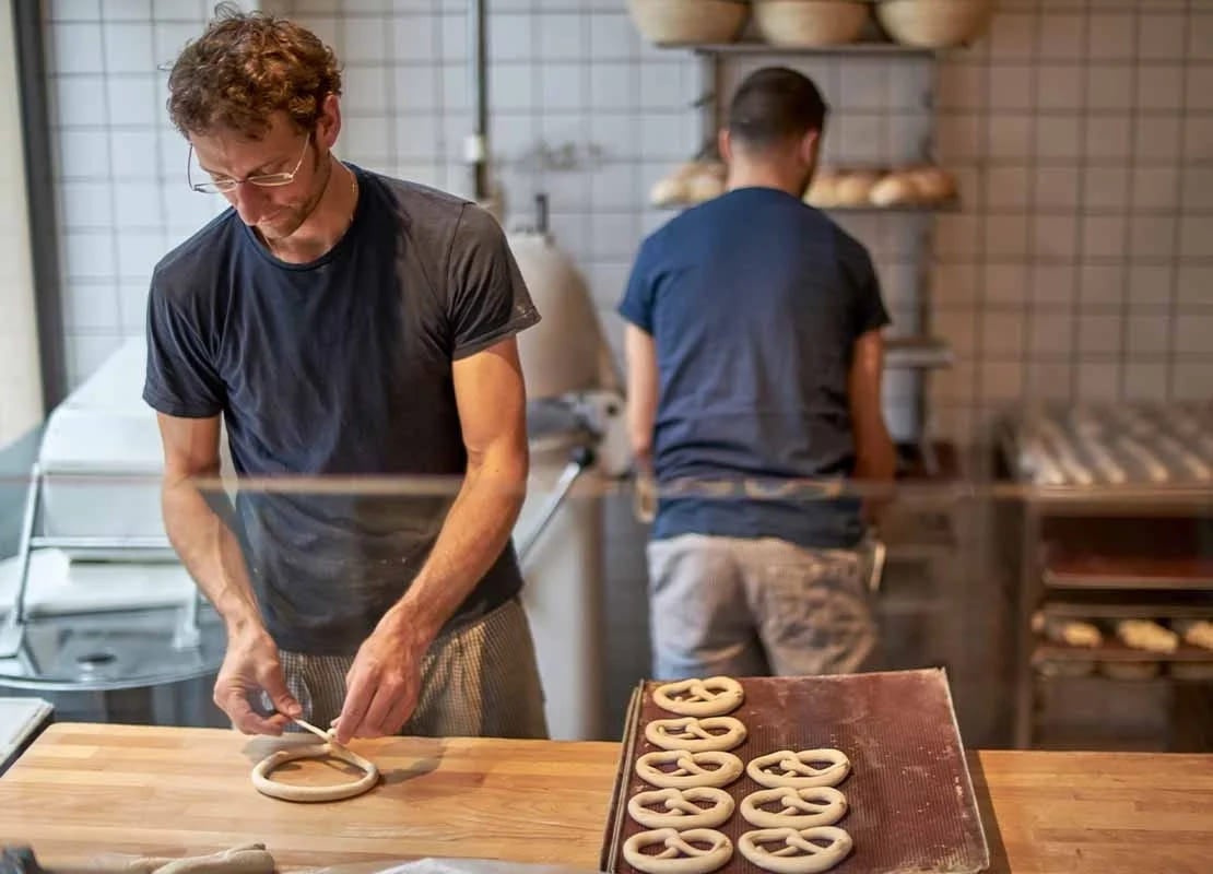 Hombres preparan en una cocina pretzels destinados a una mesa para postres con opciones balanceadas