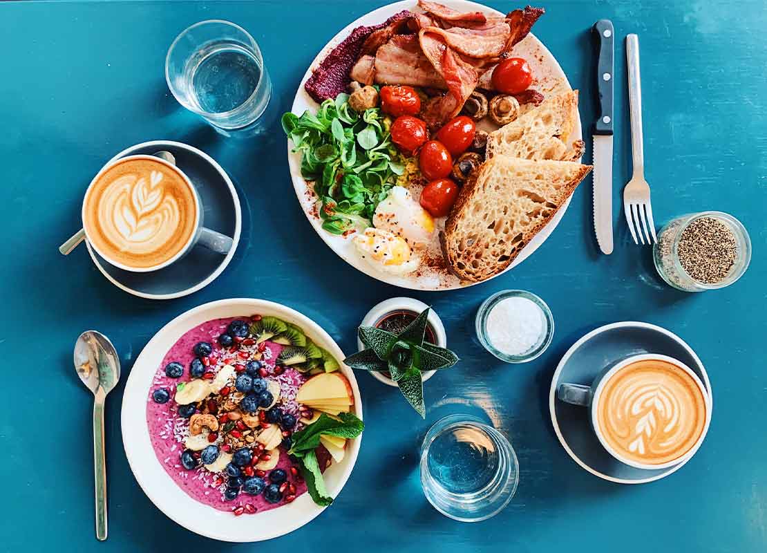 Desayunos para dos con café que hace buen maridaje con platos de fruta, yogurt, huevo, tocino, pan y tomates cherries