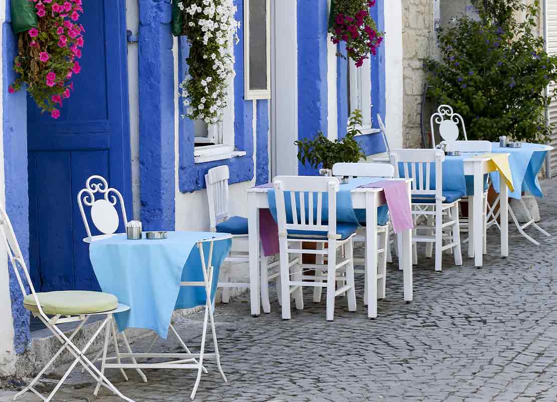 Sillas y mesas en el exterior de un restaurante temático ambientado con el estilo de la cultura mediterránea