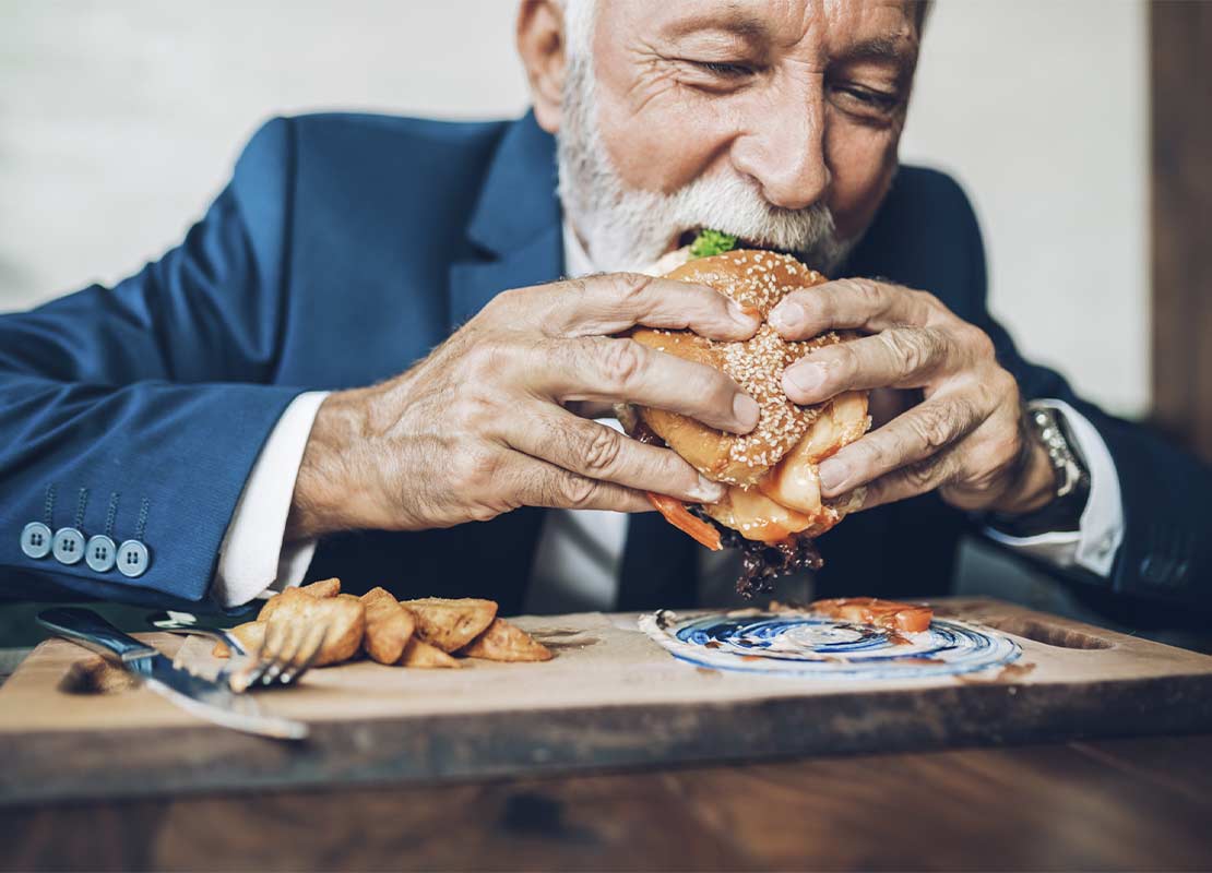 Hombre come una hamburguesa con papas en restaurante temático fast casual que combina comida rápida y orgánica