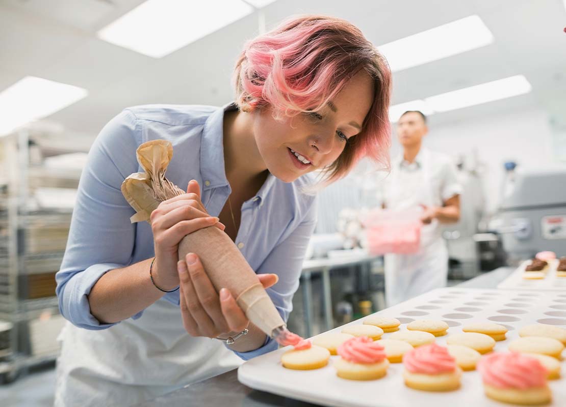 En una cocina comercial, repostera utiliza una manga para decorar con crema postres en una mesa para un servicio de catering