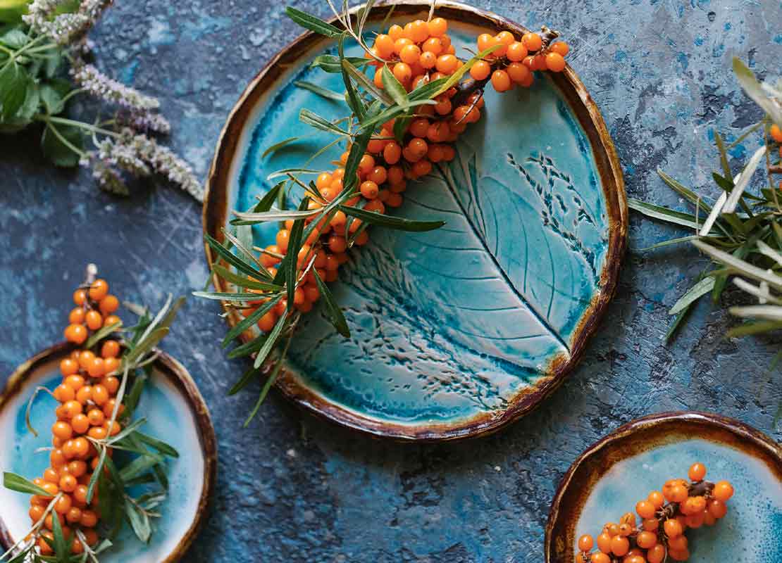 Vayas naranjas, ramas y platos de cerámica sobre mesa azul son elementos para la decoración de restaurantes