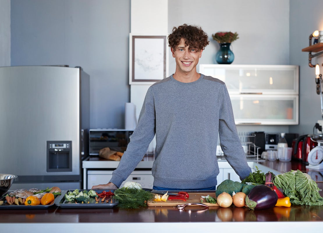 Detrás de una mesa con verduras, un influencer gastronómico mira al frente y se preparara para hacer un video en su cocina
