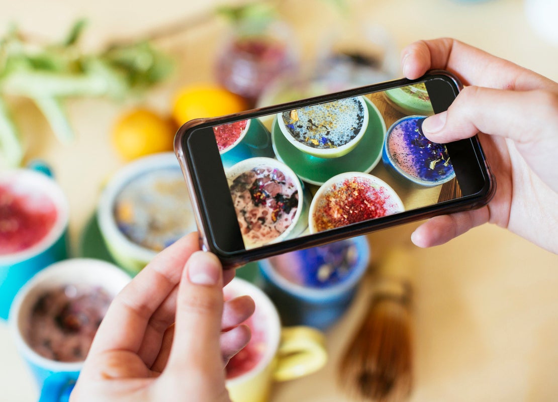 Manos de una influencer gastronómico sostienen un smartphone mientras capturan la foto de varias bebidas de colores