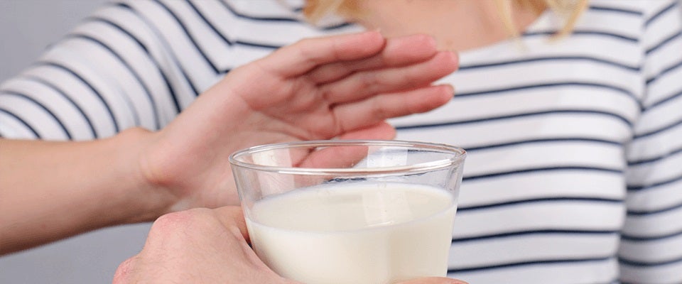 Mano de mujer rechaza vaso de leche porque es intolerante a la lactosa