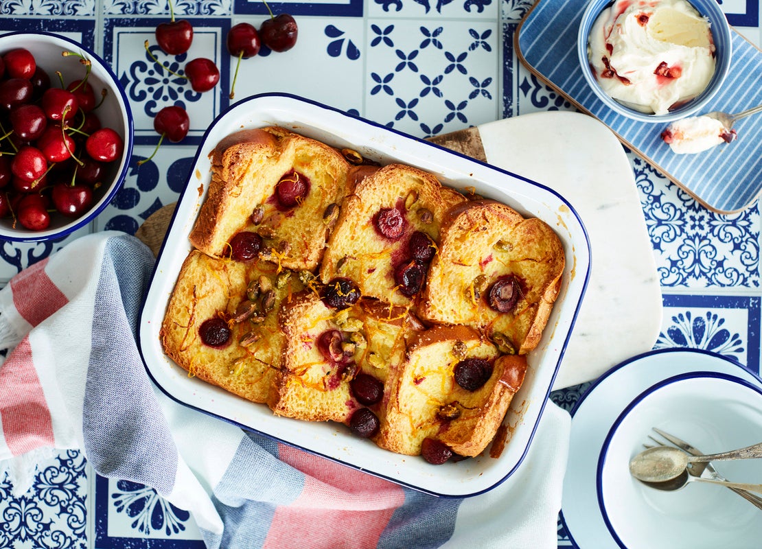 Bandeja de aluminio con 6 torrijas decoradas con fruta y mantequilla y alrededor una taza con cerezas y otra con helado