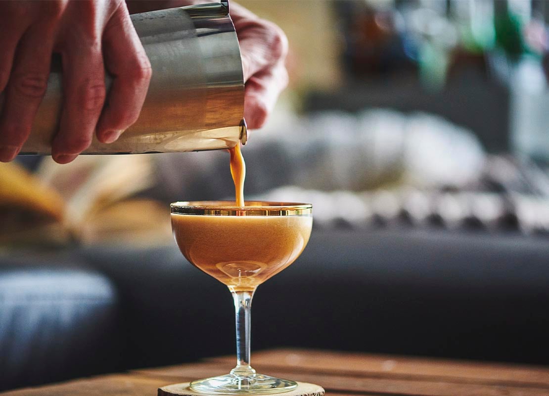 Manos masculinas sirven de una coctelera un cóctel espresso martini NESCAFÉ® en una copa