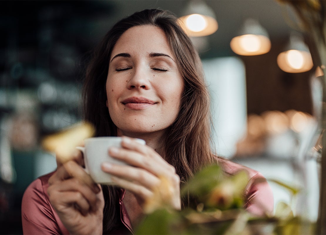Clienta de una cafetería disfruta con los ojos cerrados del aroma de una bebida mientras sostiene con las dos manos una taza