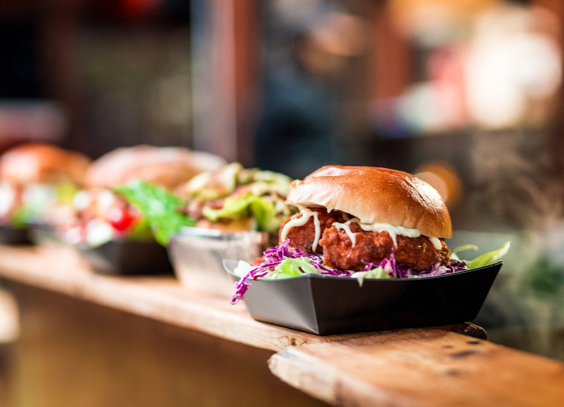 Hamburguesas con albóndigas de cerdo fritas en una taza cuadrada, expuestas y a la venta sobre una repisa de en un food hall