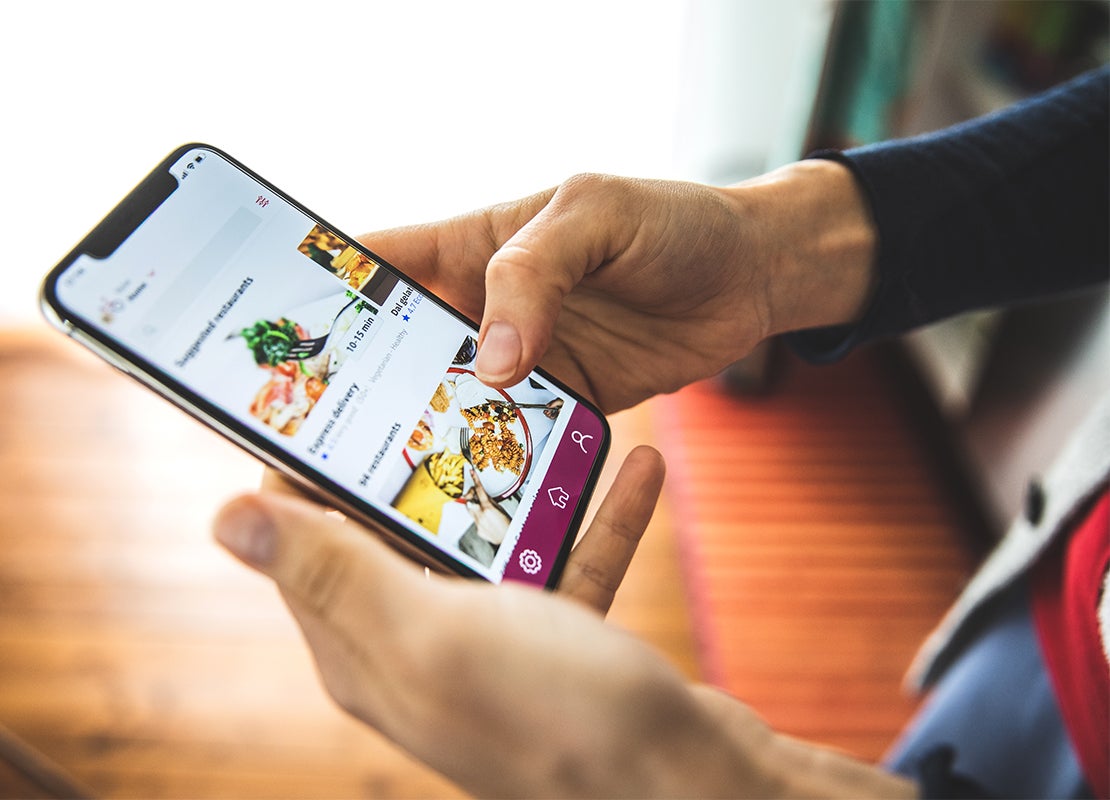 Manos de una mujer sostienen un celular en el que pide comida a domicilio a través de una app