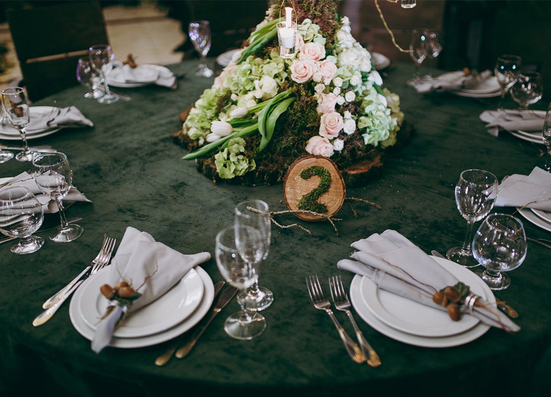 Mesa redonda puesta con platos, cubiertos, copas y servilletas para los invitados de una boda con un centro de mesa de rosas