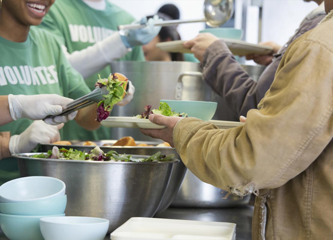 Personas con camisetas de color verde sirven alimentos en un comedor comunitario