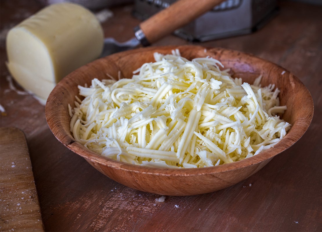 Plato hondo de bambú que contiene queso rallado, junto a otros instrumentos de este material sobre una mesa