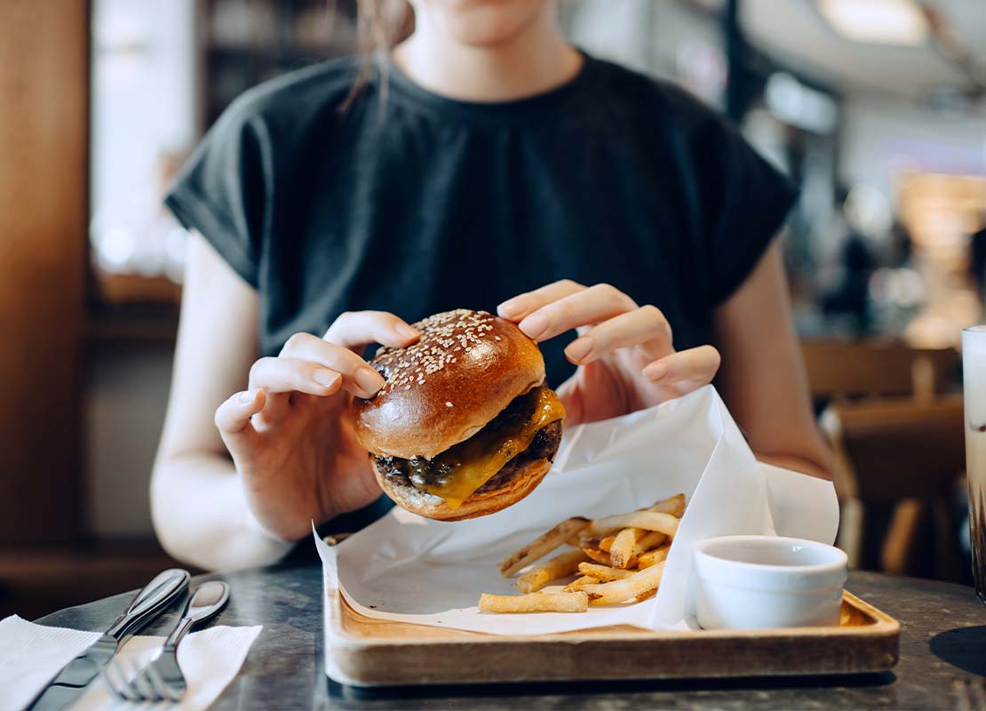 Mujer sostiene en sus manos una hamburguesa sencilla coronada con salsa BBQ