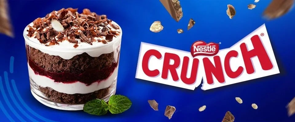 Postre Trifle en un vaso del que se aprecian sus capas de crema y bizcocho, decorado con CRUNCH® troceado