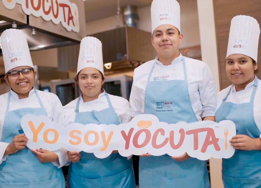 Cuatro estudiantes del Programa YOCUTA sostienen un letrero mientras posan para una foto
