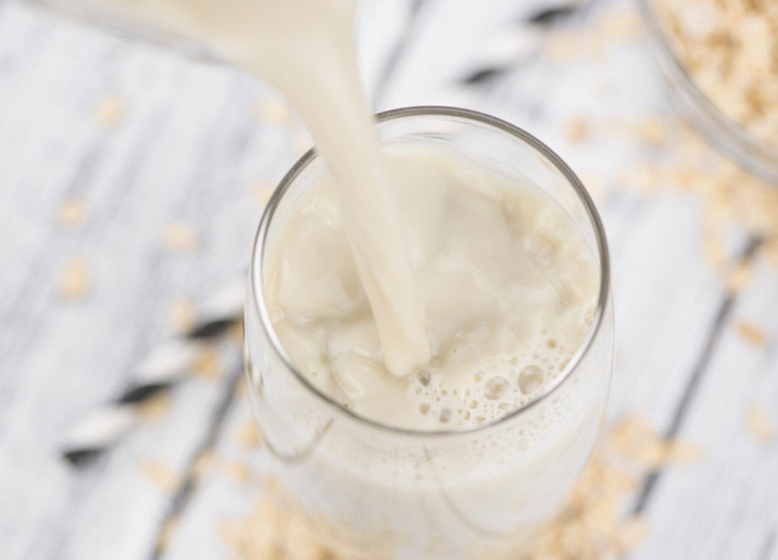 En un vaso sobre una mesa de madera se sirve bebida vegetal de avena