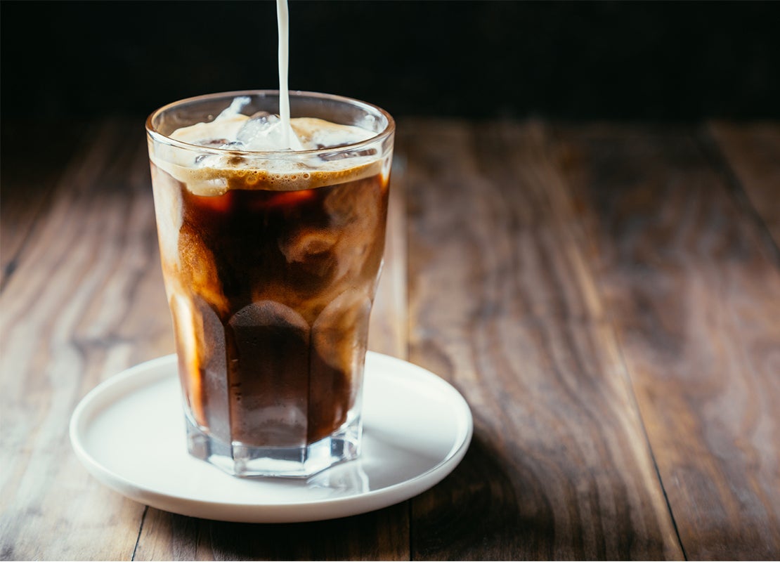 Vaso de café frío preparado con NESCAFÉ®, cubos de hielo y una bebida vegetal la cual se está vertiendo
