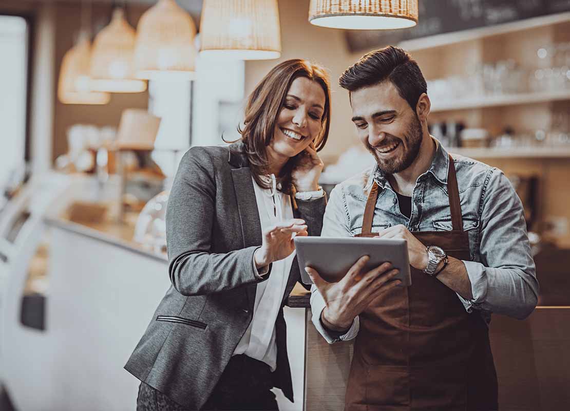 Dueña de una cafetería y barista revisan en una tablet un estudio de mercado en el establecimiento
