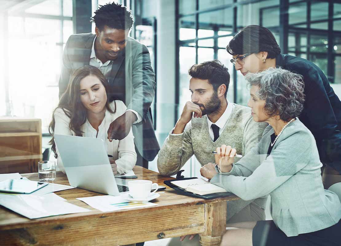 Hombre señala un portátil para explicar un estudio de mercado a su equipo de trabajo en una oficina