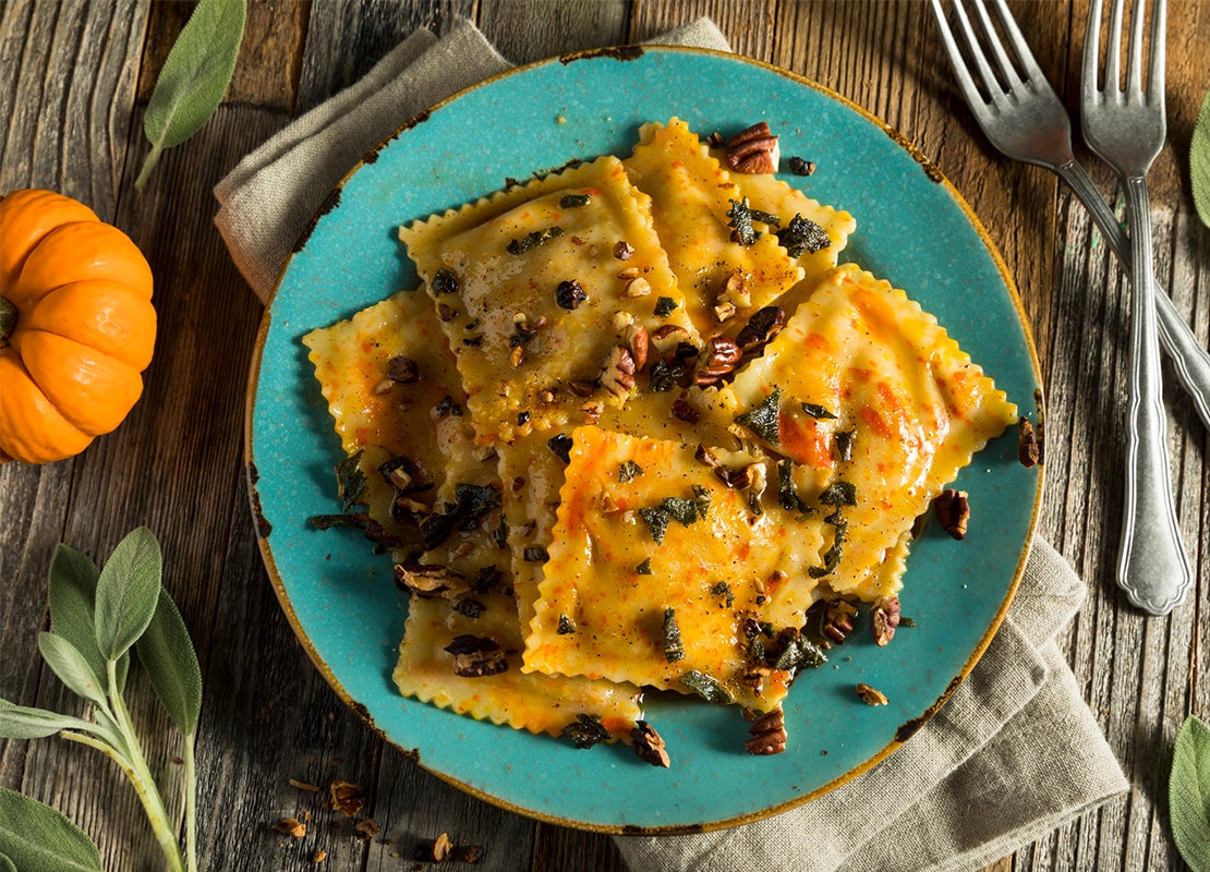 Raviolis de calabaza con salsa de frutos secos y ajedrea en un plato azul y alrededor sus ingredientes