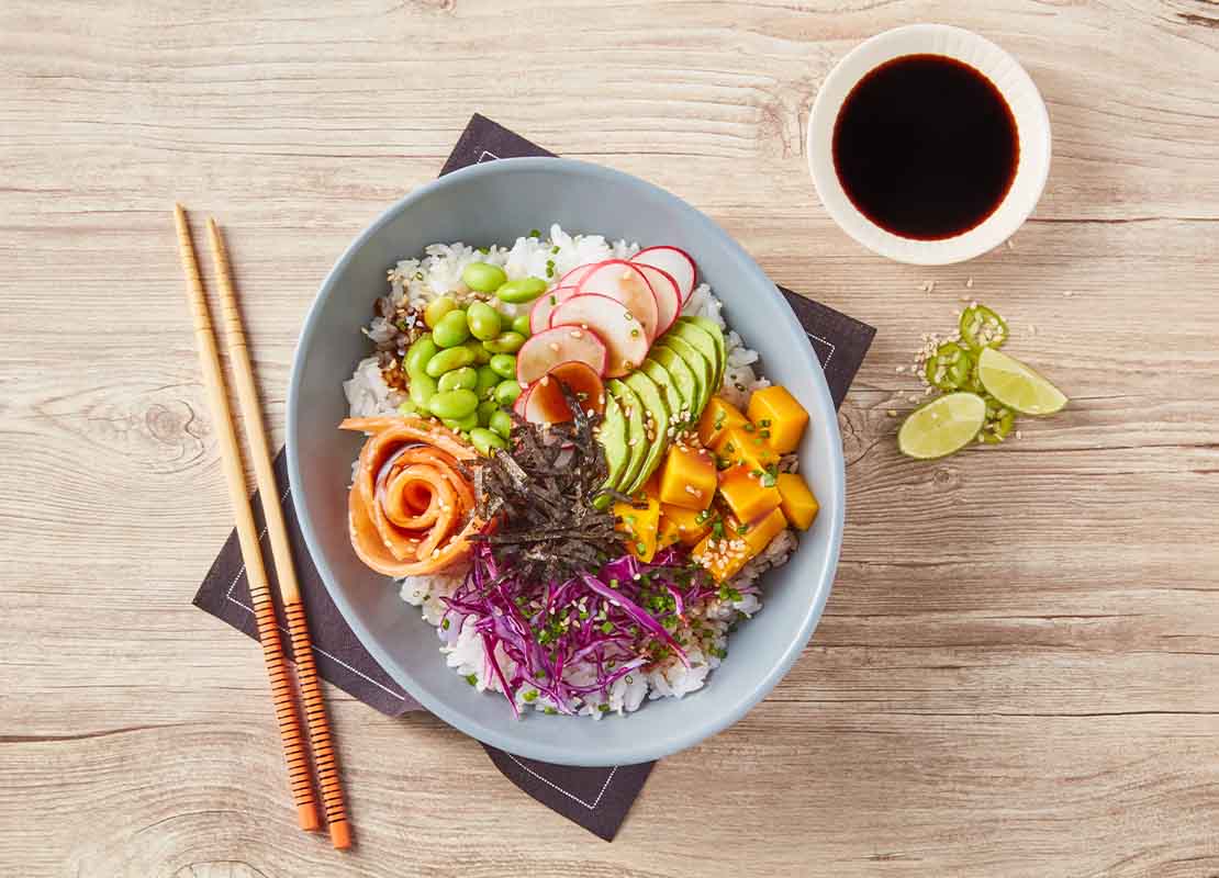 Poke bowl compuesto de arroz, vegetales y pescado acompañado de salsa de soya, una receta umami