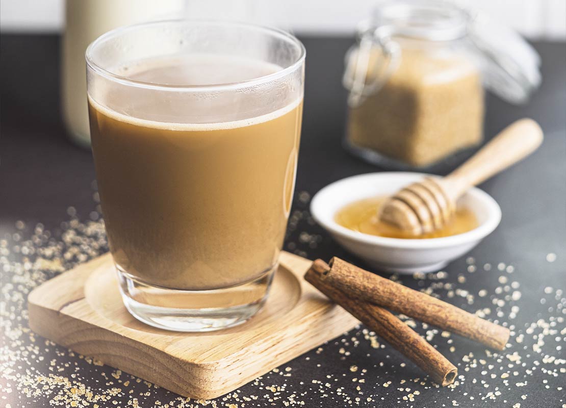 Vaso de café latte rodeado de ingredientes para añadir sabor como miel, canela y azúcar