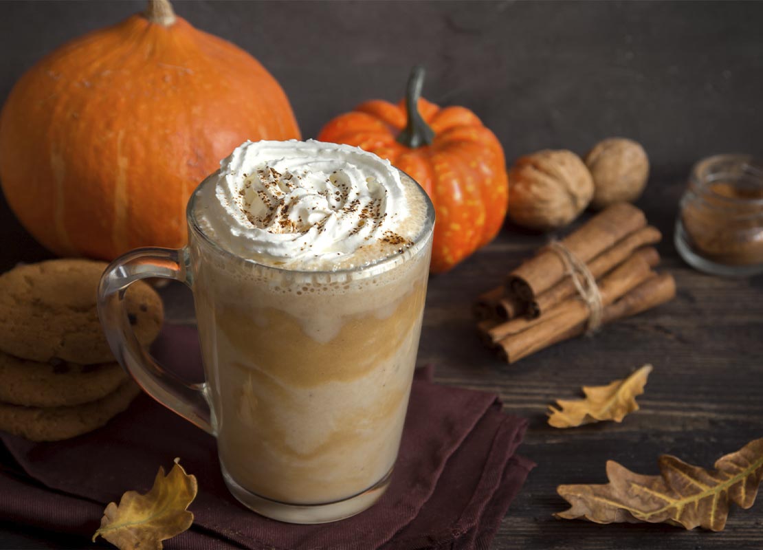 Pumpkin spice latte rodeado de decoración otoñal como especias de temporada, galletas y calabazas