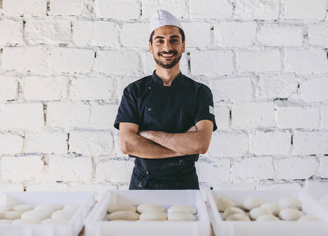 Chef cruzado de brazos tras cajas con masas para hacer pizzas en un negocio de comida
