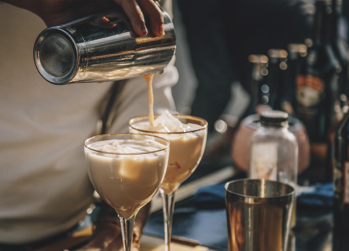 Manos de mixólogo vierten mezcla de cóctel de café sin alcohol en dos copas, como parte de las food trends