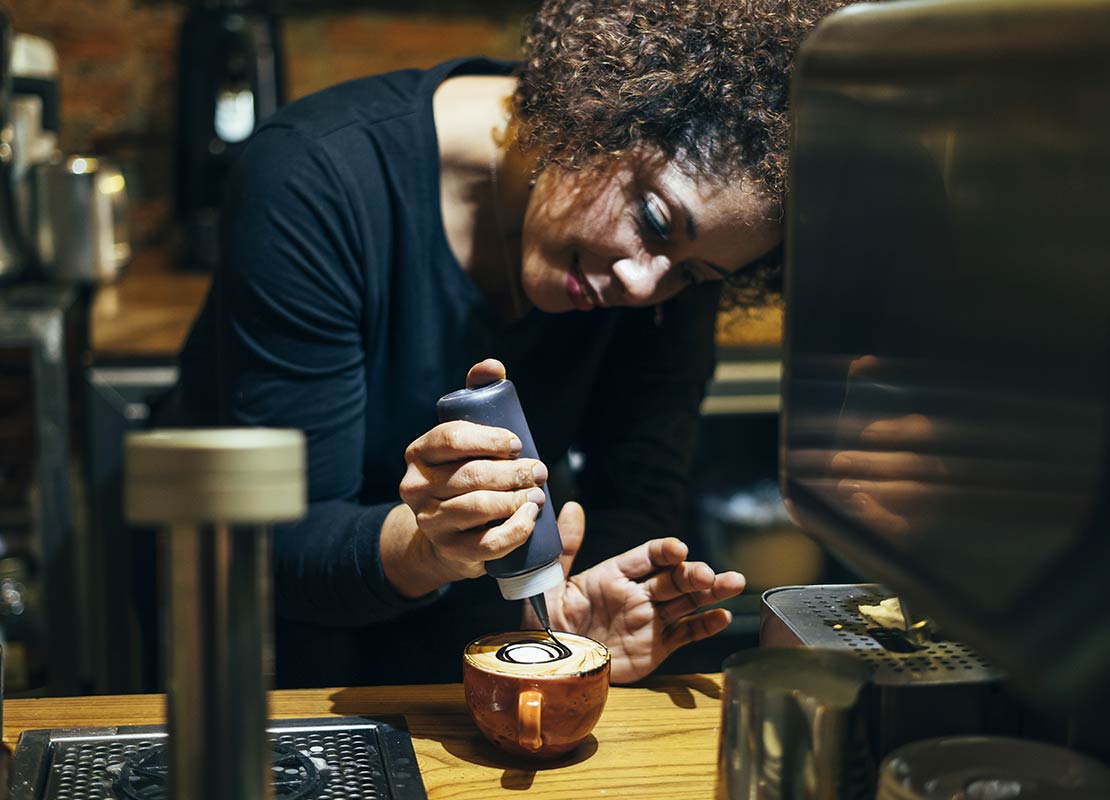 Barista decora con cuidado una bebida con un sirope de chocolate en una cafetería